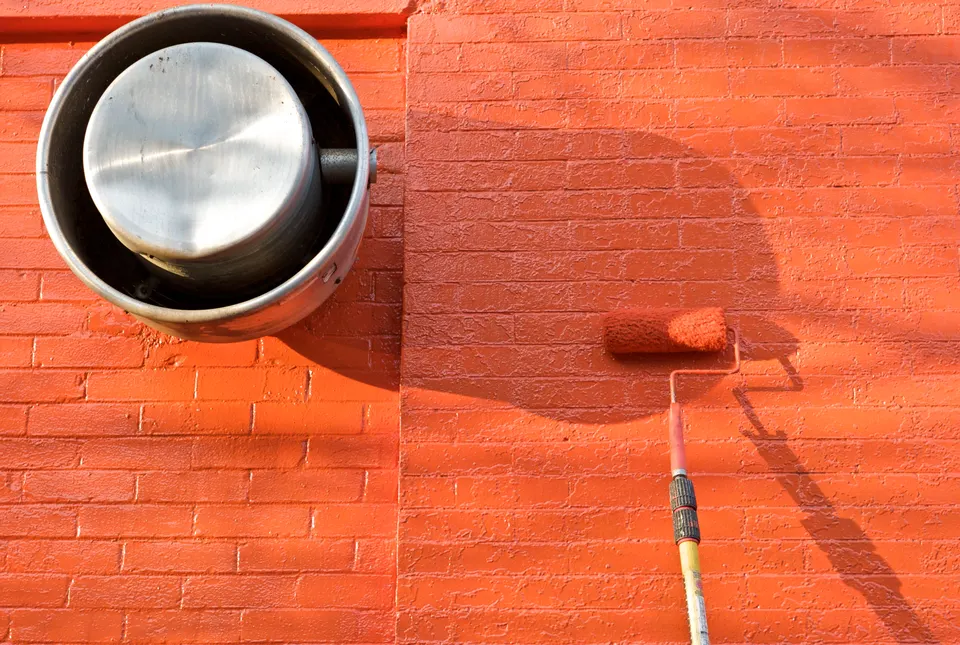 Paint roller applying orange paint to a brick wall